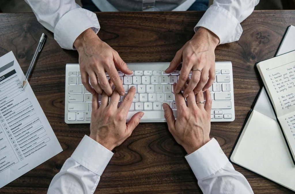 Vue aérienne des mains sur un clavier mécanique avec une fiche de référence des raccourcis clavier imprimée sur un bureau en bois